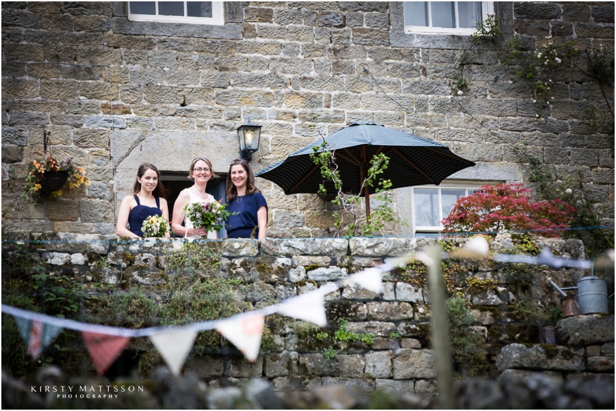 Four bridesmaids standing on a stone wall with umbrellas.