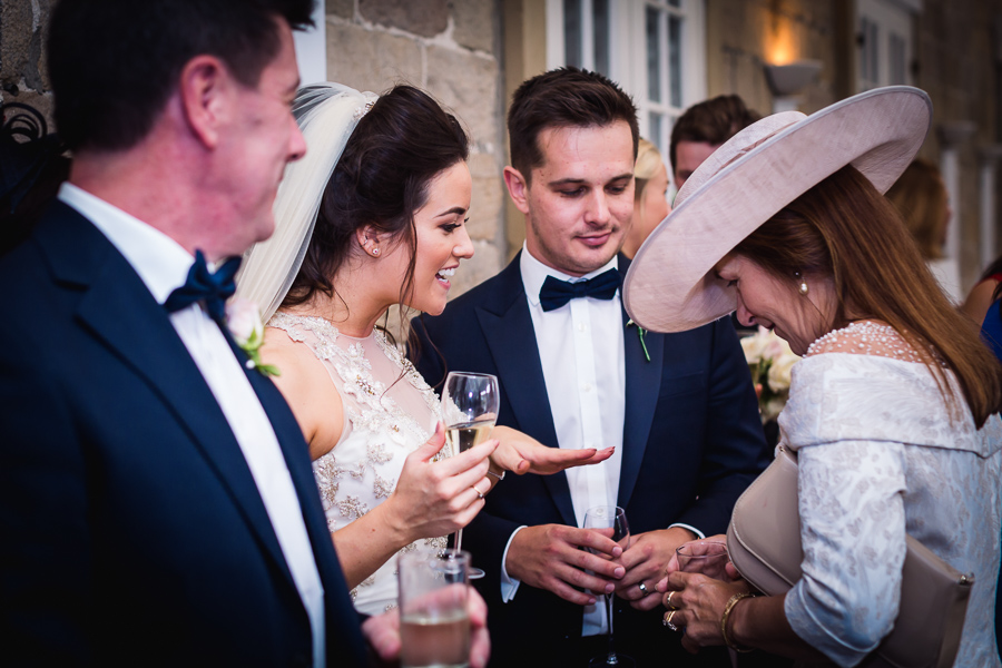 A wedding party engaging in conversation and toasts, with a bride holding a champagne glass smiling at her guests.