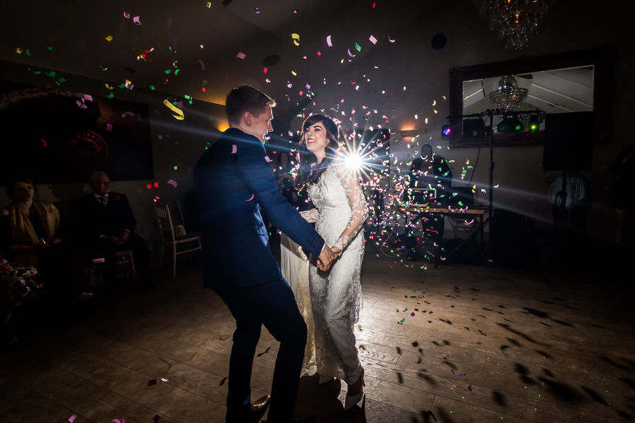 Couple dancing amidst confetti with a light flare at a wedding reception.
