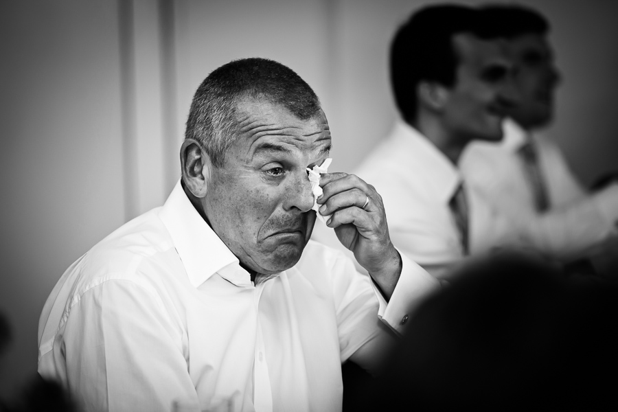 A man wiping his eye with a tissue at an indoor event.