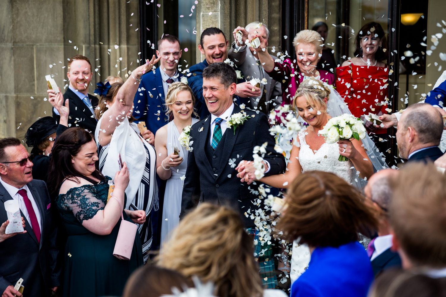 A joyful bride and groom walk through a shower of confetti, surrounded by smiling guests.