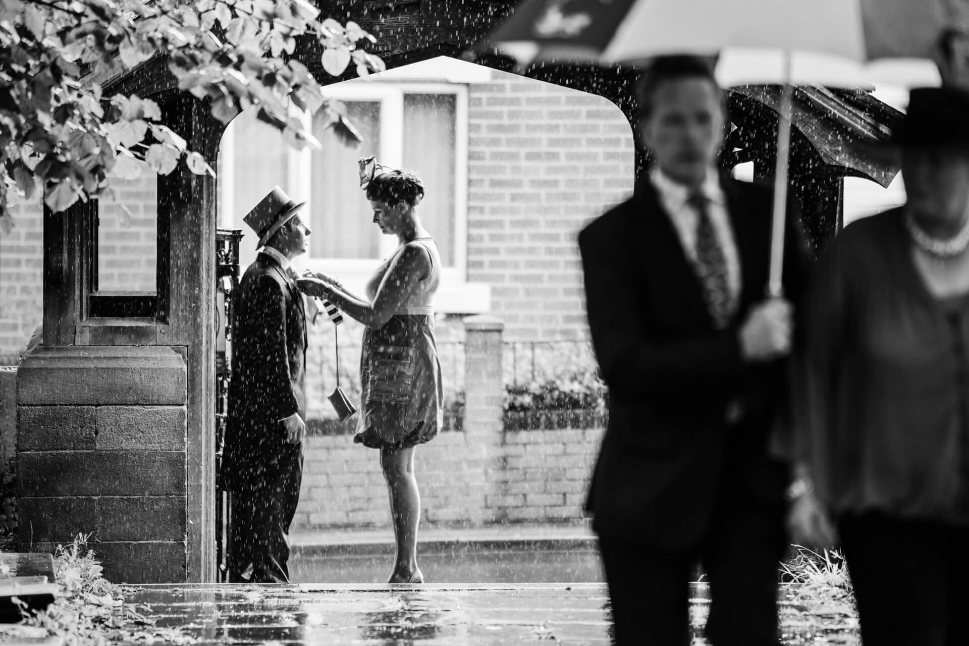 Black and white wedding photography portfolio photo of a couple walking in the rain with umbrellas.