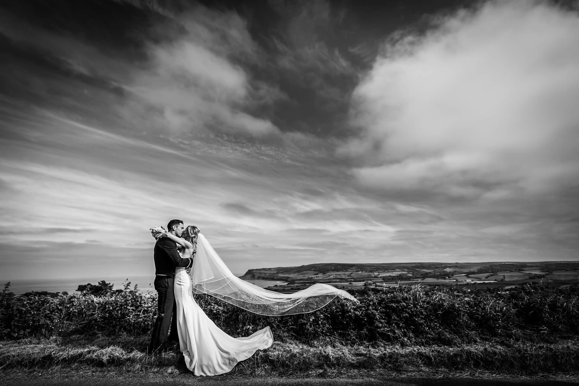 groom kissing the bride on a hill top overlooking Whitby