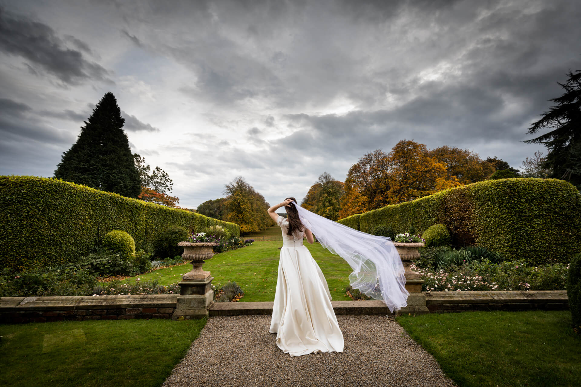 A bride is walking down a path with her veil for her wedding photography portfolio.