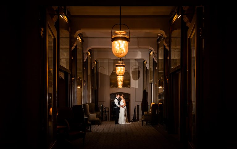A couple embracing in a warmly lit hallway with elegant hanging lanterns.