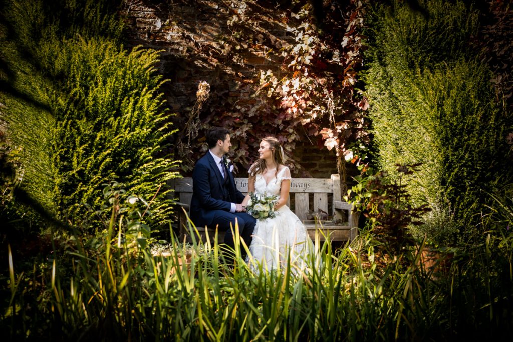 wedding couple sat on a garden bench at Saltmarshe Hall