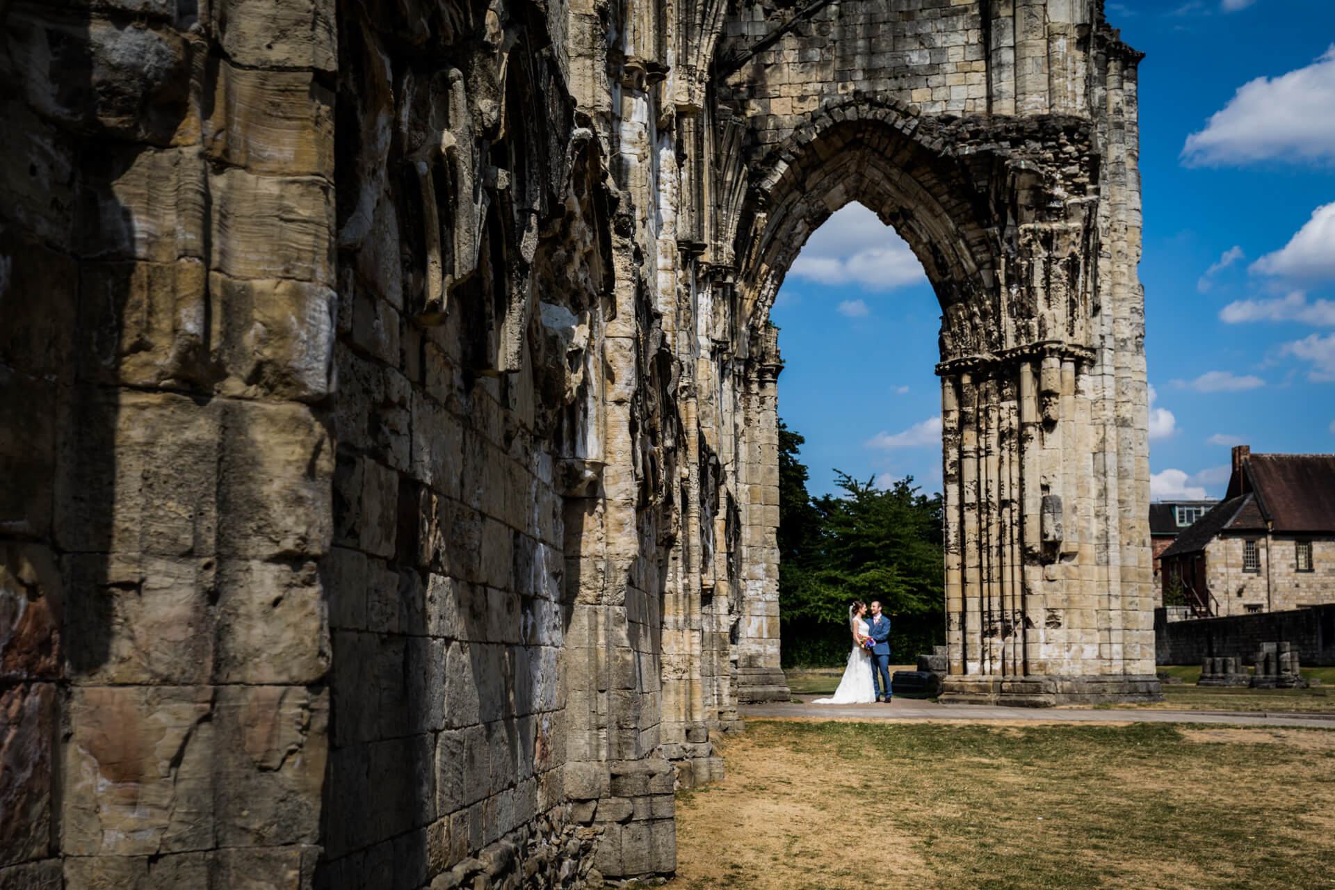 bride and groom hold hands in the archway of some run-ins in the York museum gardens