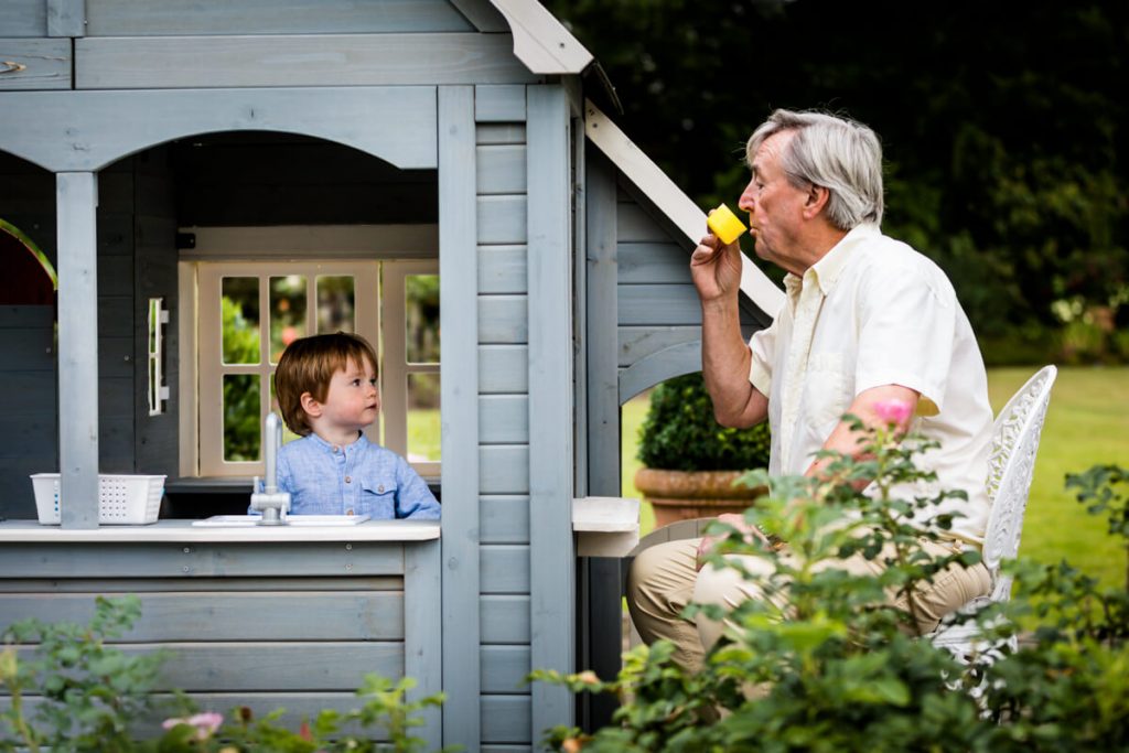 little boy serving tea to his grandfather from his play house