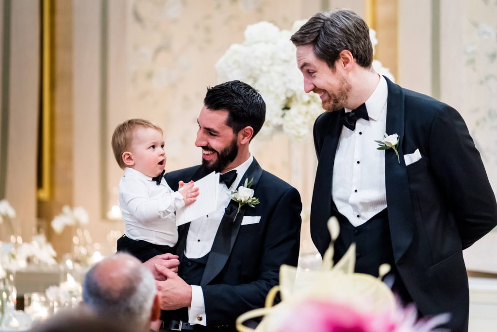 the groom and his baby boy chatting with the best man at the top of the aisle
