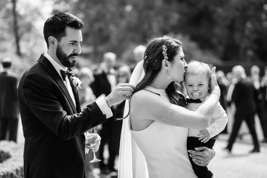 bride kissing her baby boy's head whilst the groom removes confetti from her hair