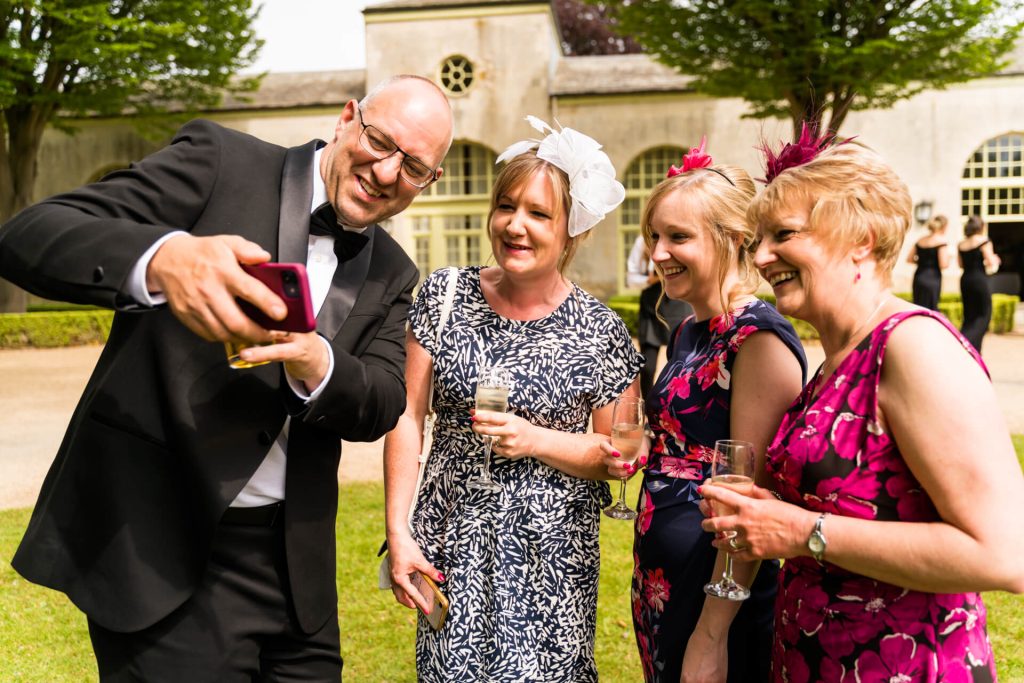 wedding guests laughing whilst looking at a phone
