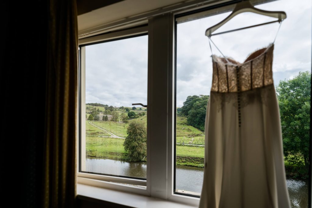 wedding dress hanging in a window overlooking the yorkshire countryside