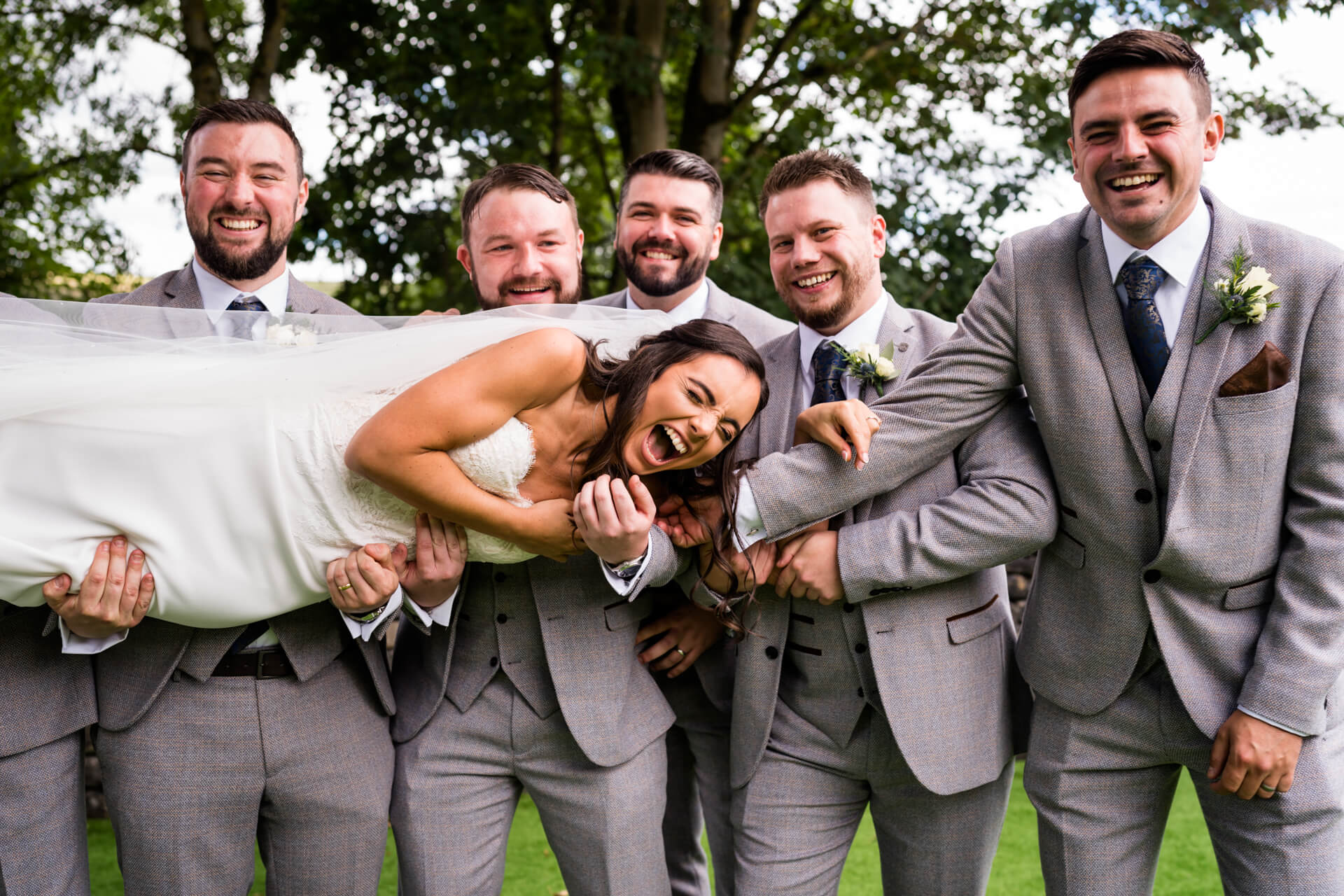bride is in hysterics as she is picked up by the groomsmen
