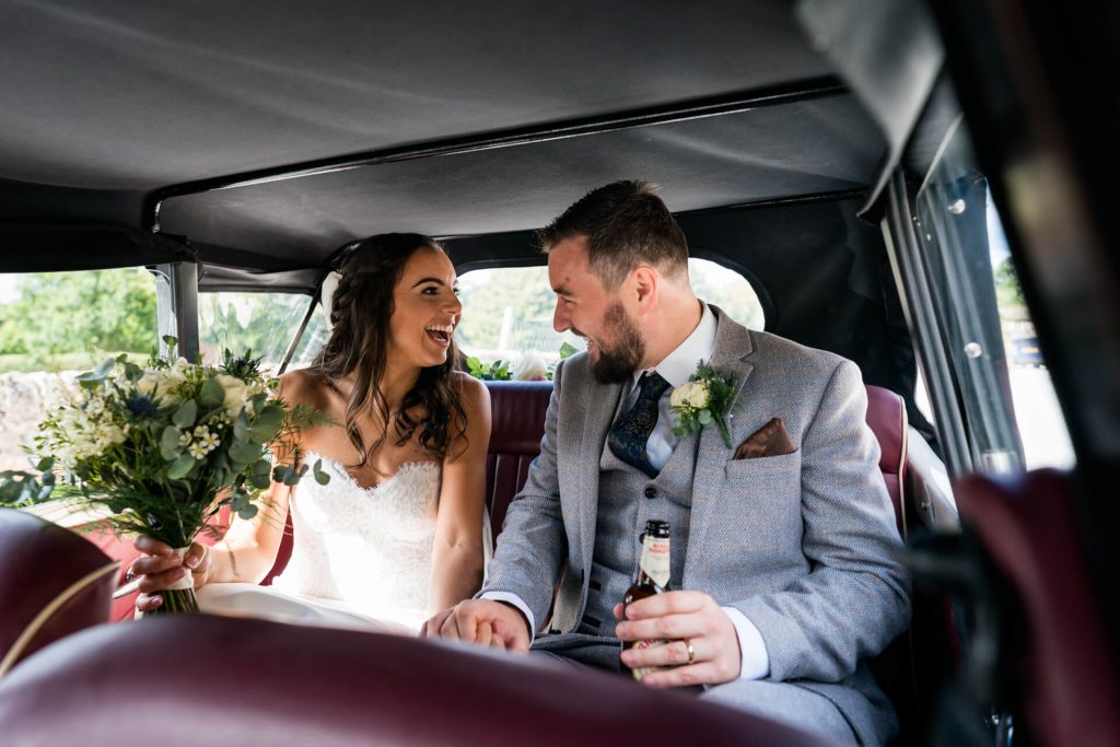 bride and groom look at each other in the wedding. car and laugh