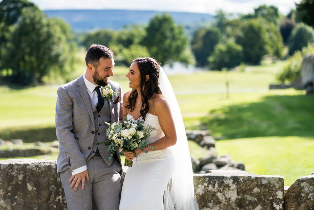 wedding couple sit on a wall and smile at each other