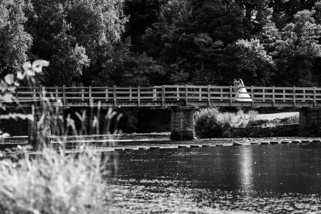 wedding couple walk across a bride over a river at Bolton Abbey
