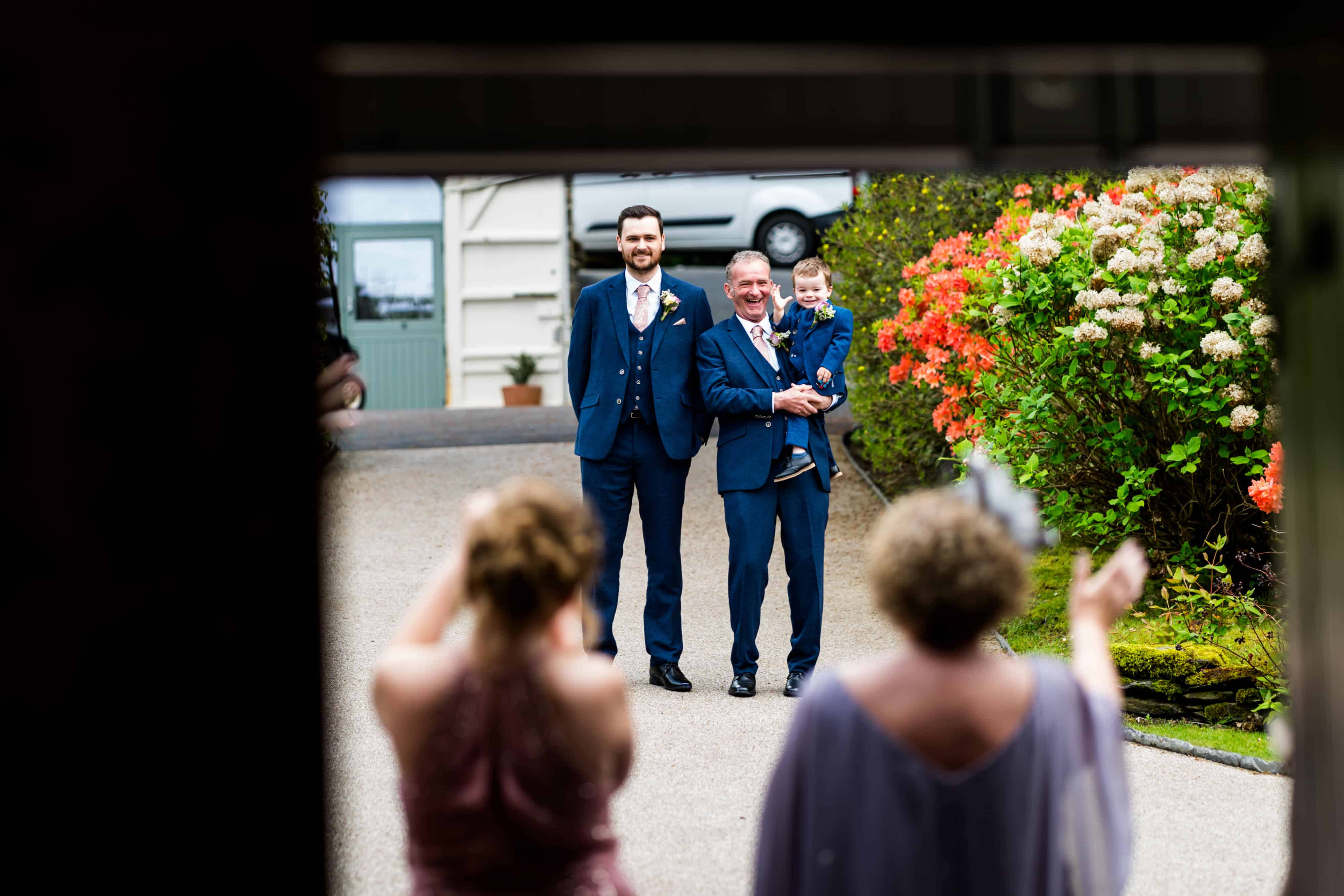 Wedding guests waving and a a little page boy waving back whilst being held by his grandpa