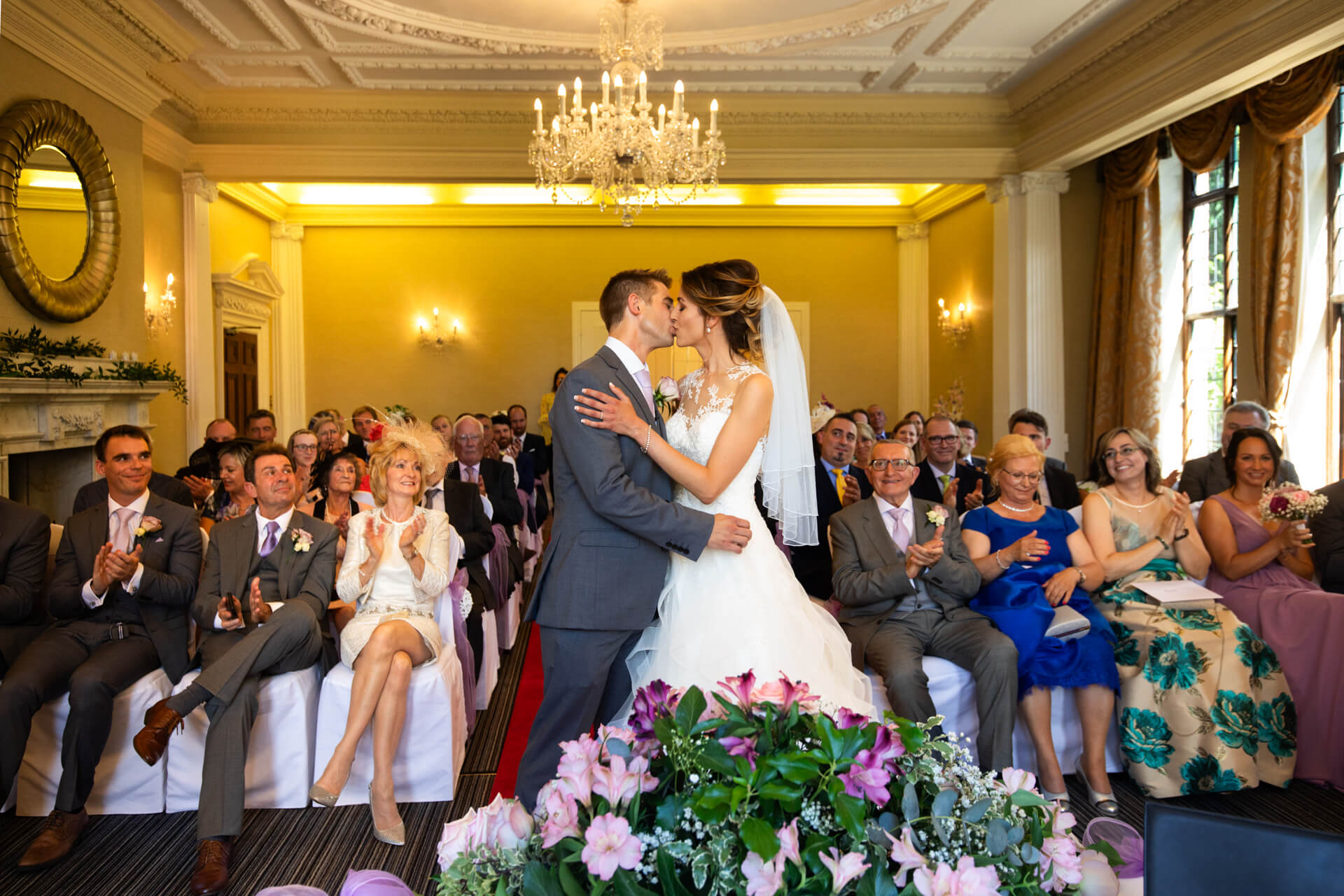 Bride and groom kissing at wedding ceremony at Aldwark Manor with guests
