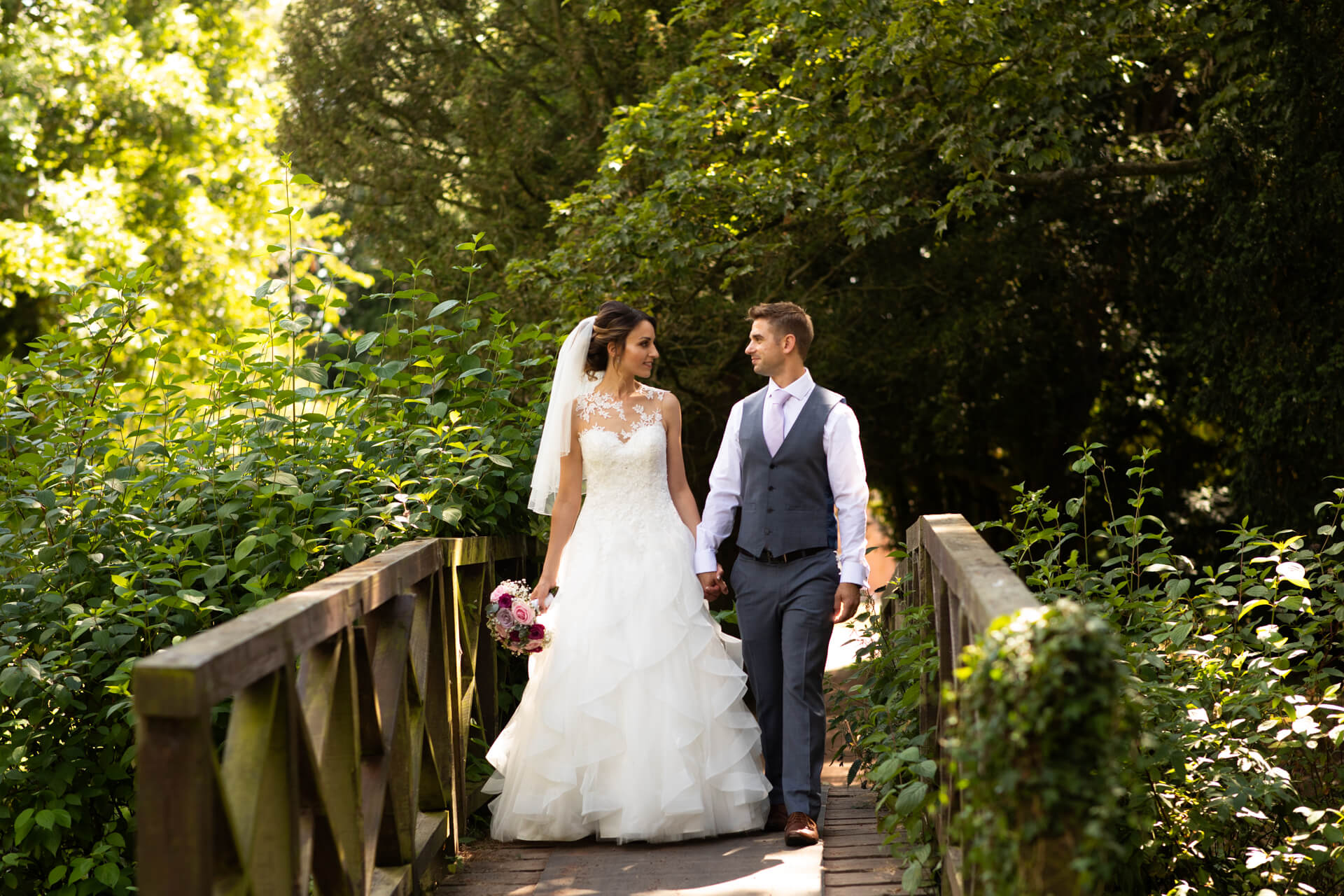Bride and groom walking on a wooden bridge outdoors.