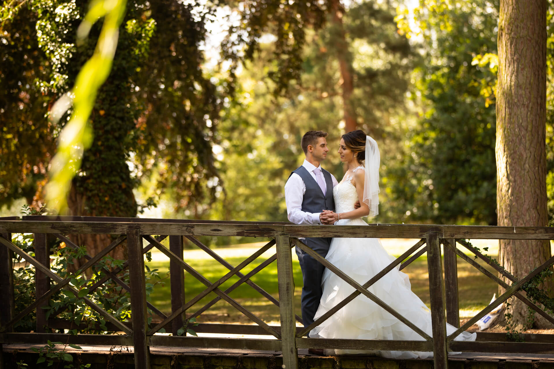 Bride and groom on bridge in sunny garden at Aldwark Manor
