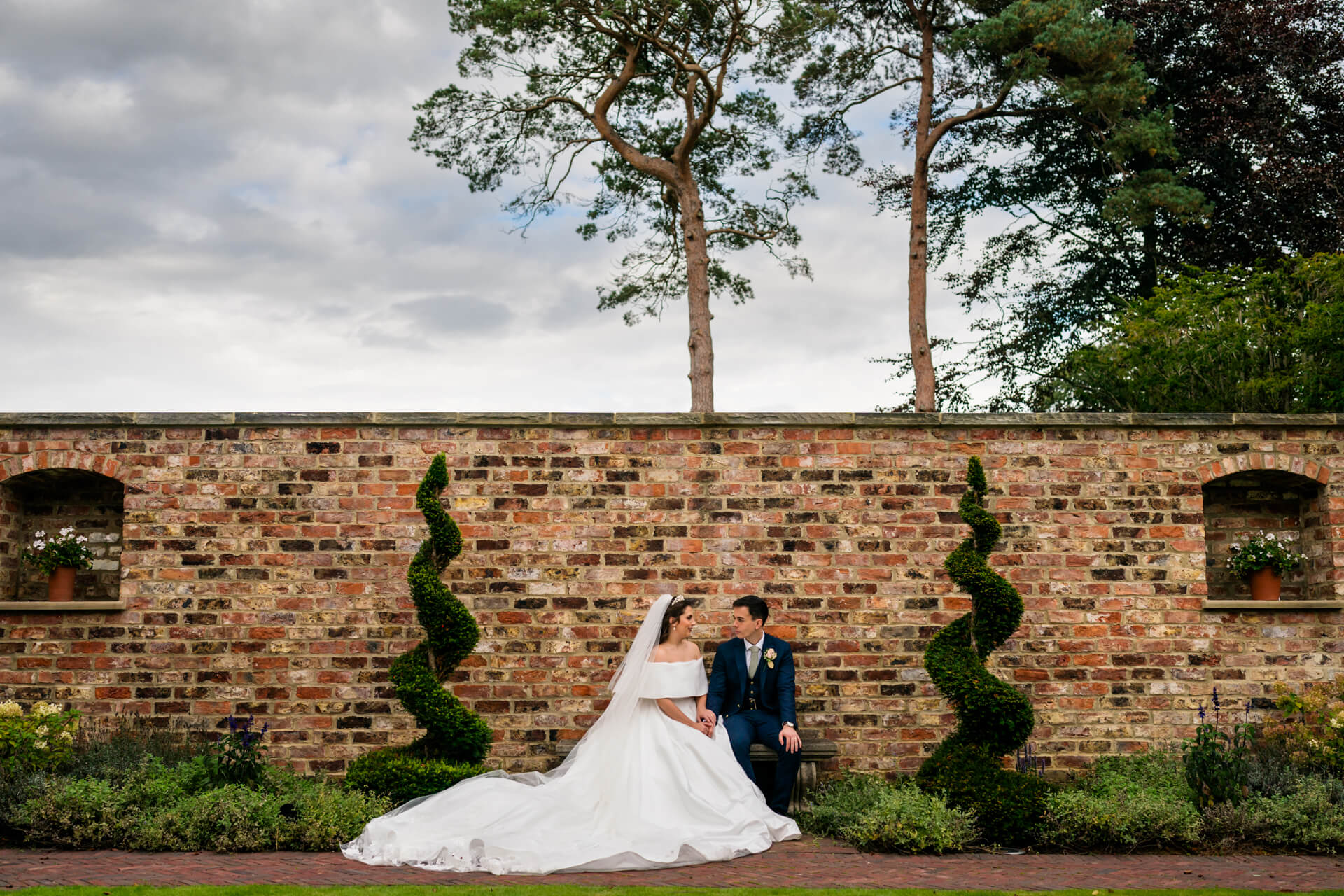 Bride and groom sitting by brick wall outdoors.