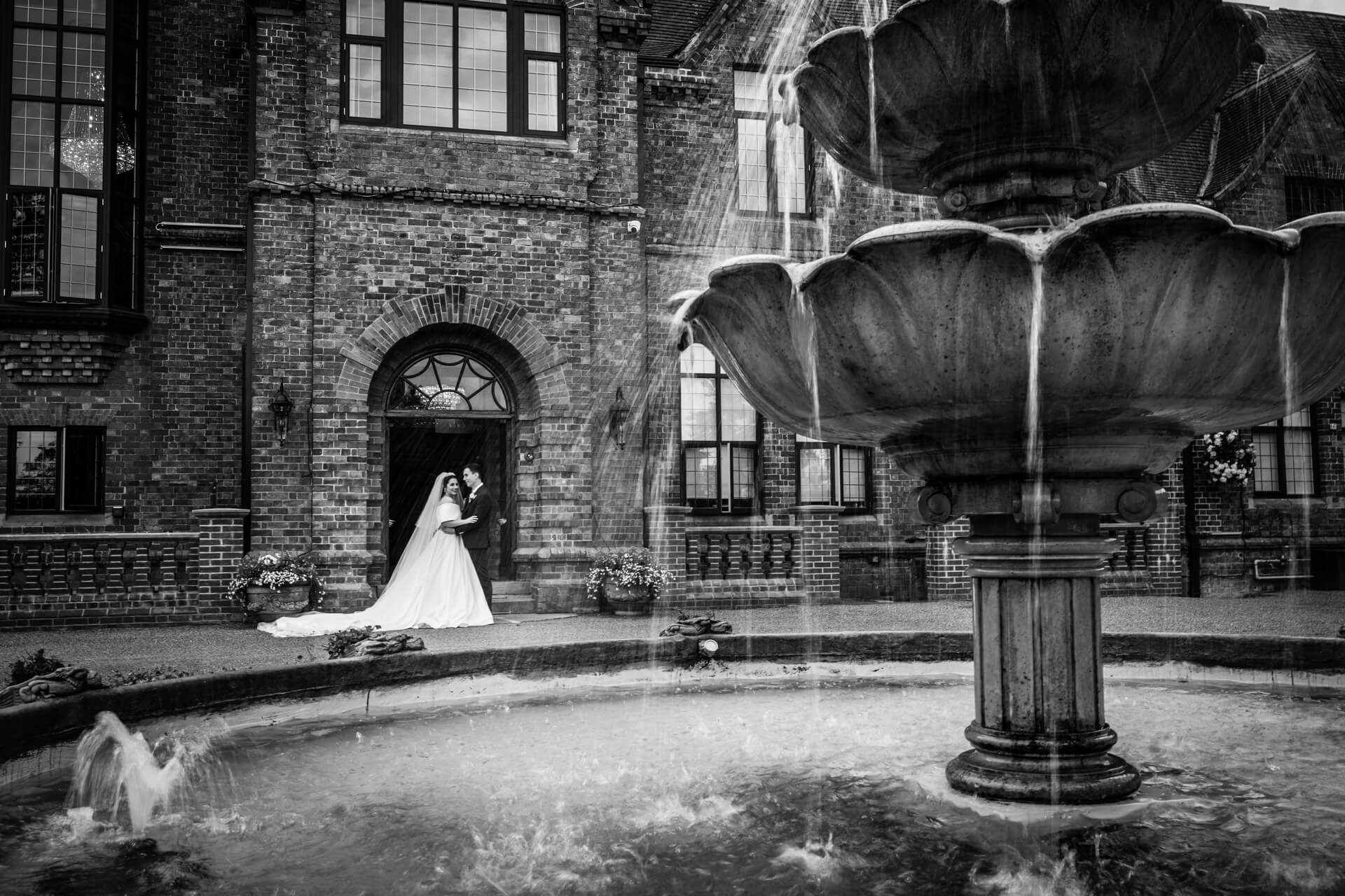 Bride and groom by Aldwark Manor fountain in monochrome.