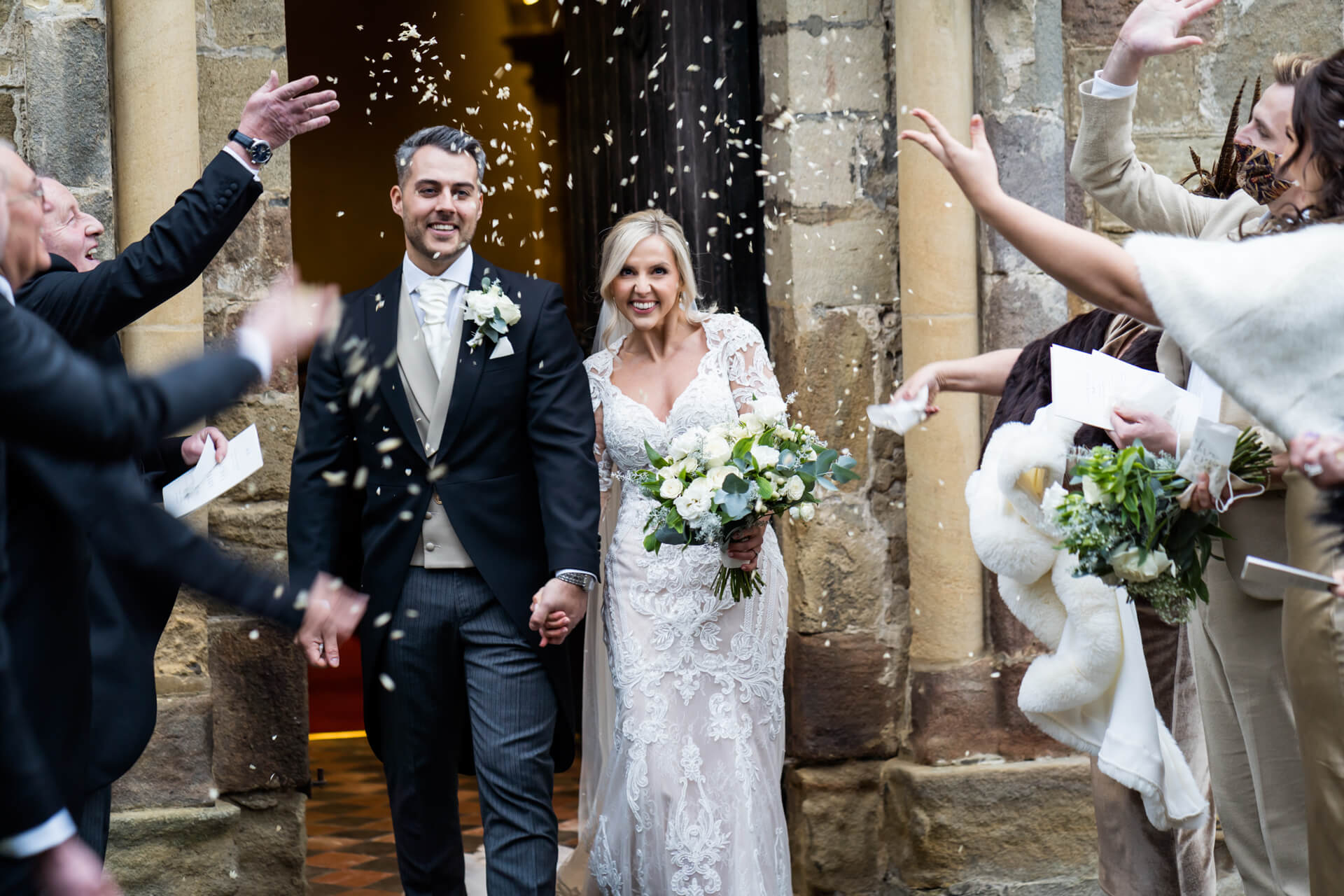 Bride and groom with guests throwing confetti at wedding.