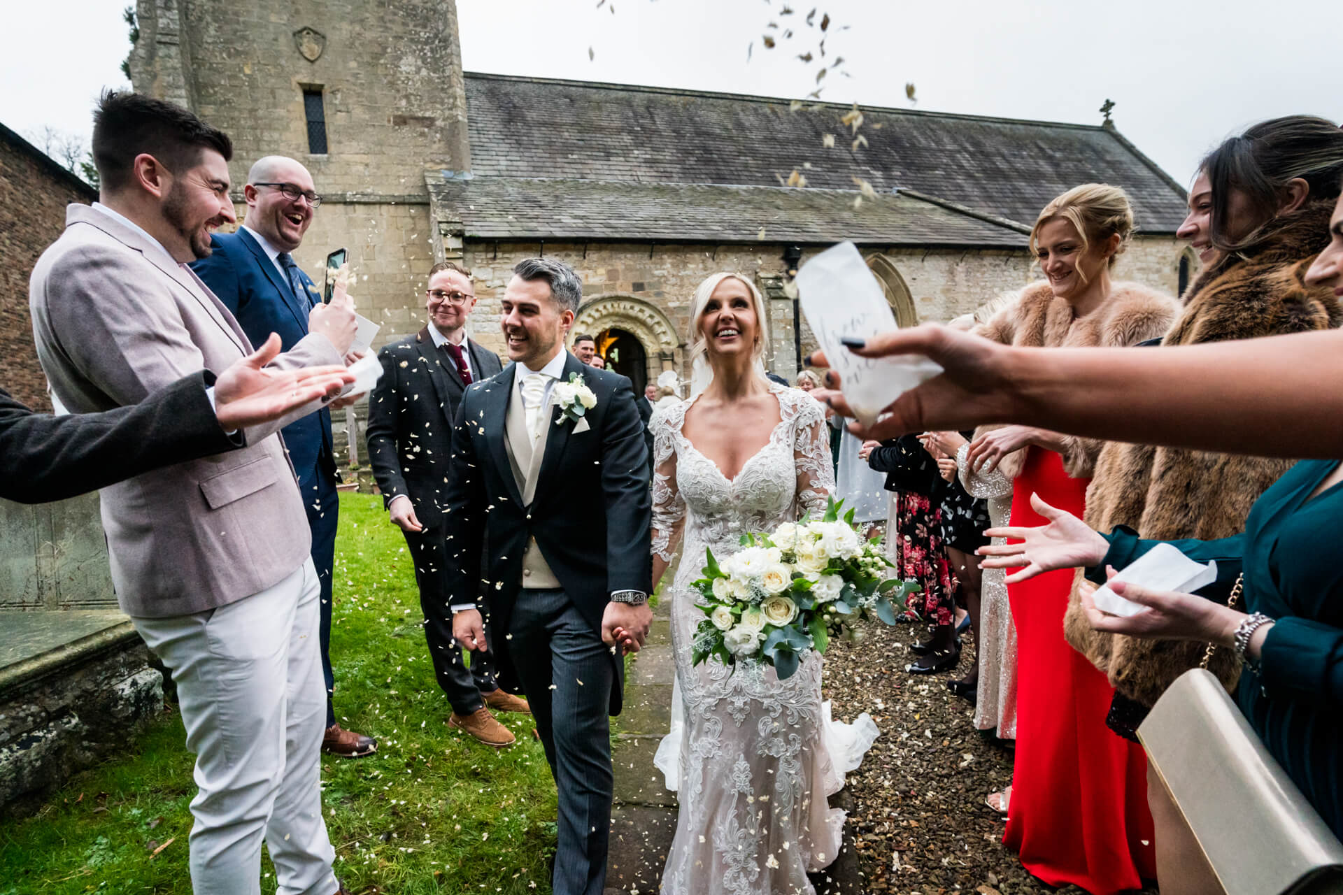 Bride and groom walking under confetti toss at wedding at Goldsborough church