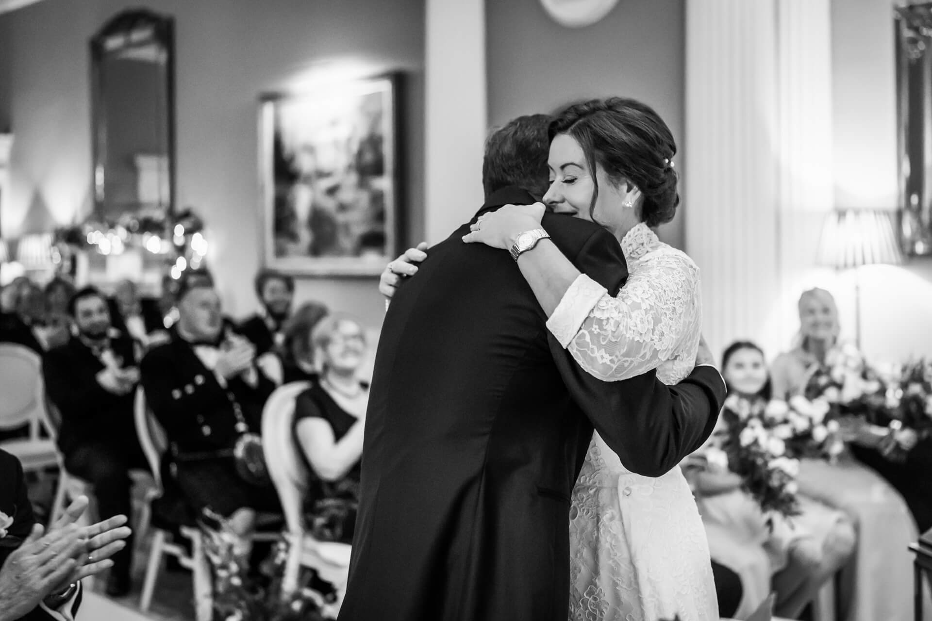 Emotional wedding hug, couple, guests applauding, black and white photo.