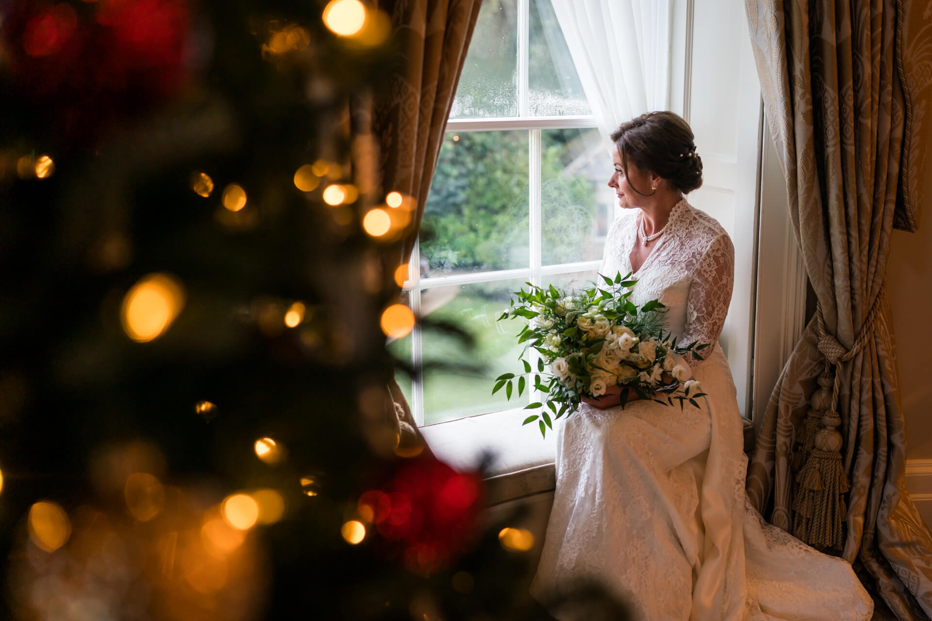 Bride with bouquet beside window at Grantley Hall , Christmas tree bokeh.