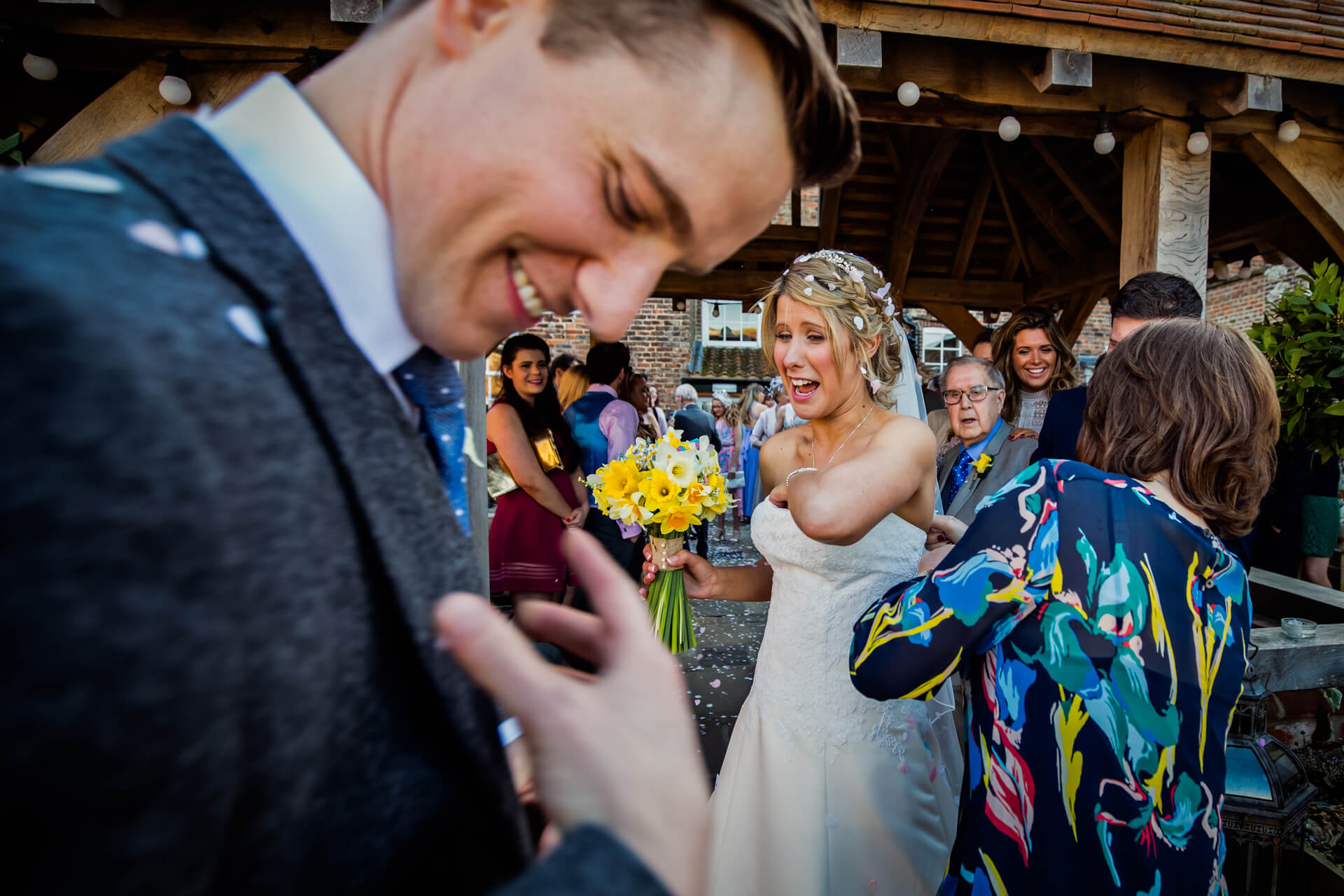 Bride and groom laughing during confetti toss at wedding.