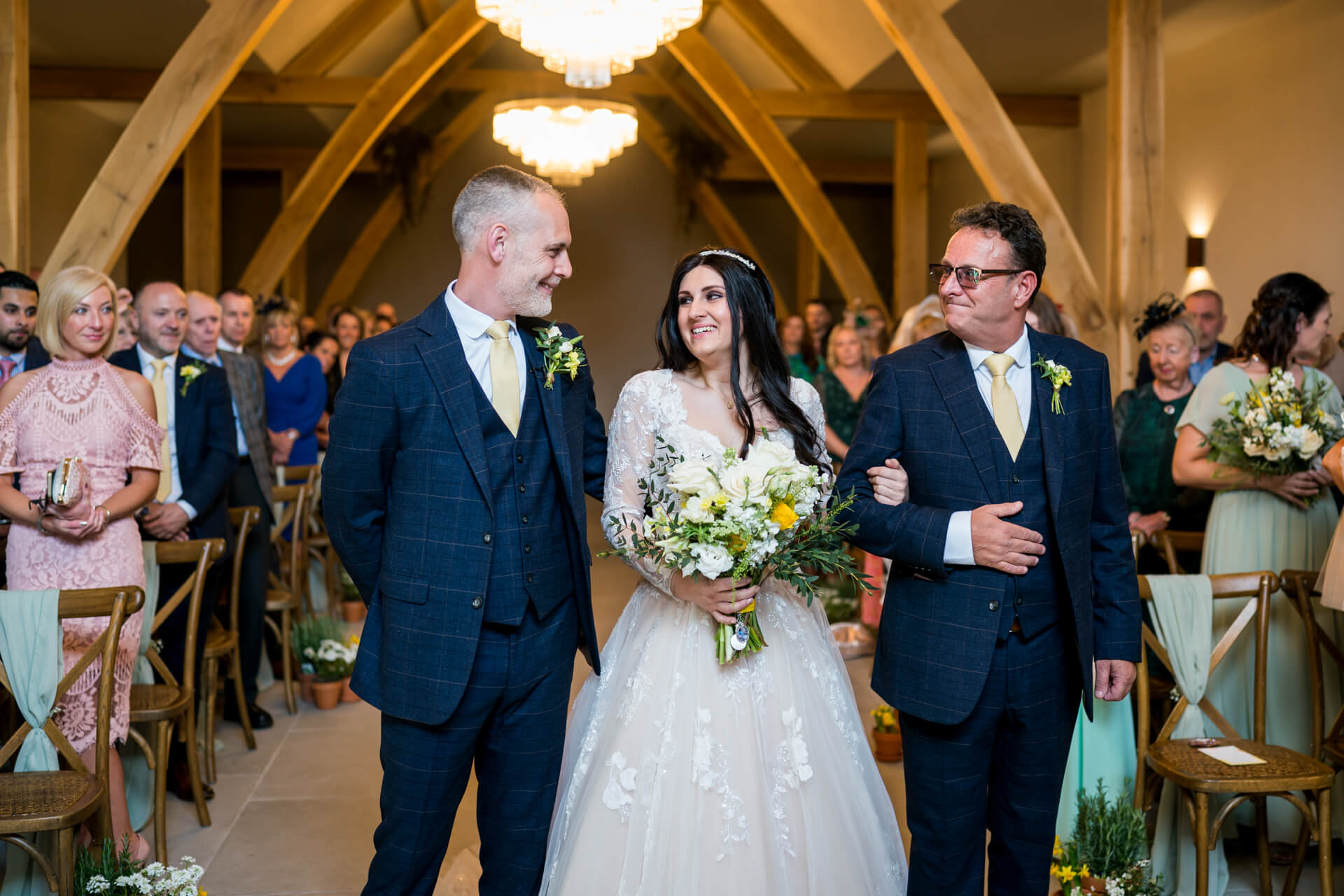 Bride walking down aisle with father, groom awaits.