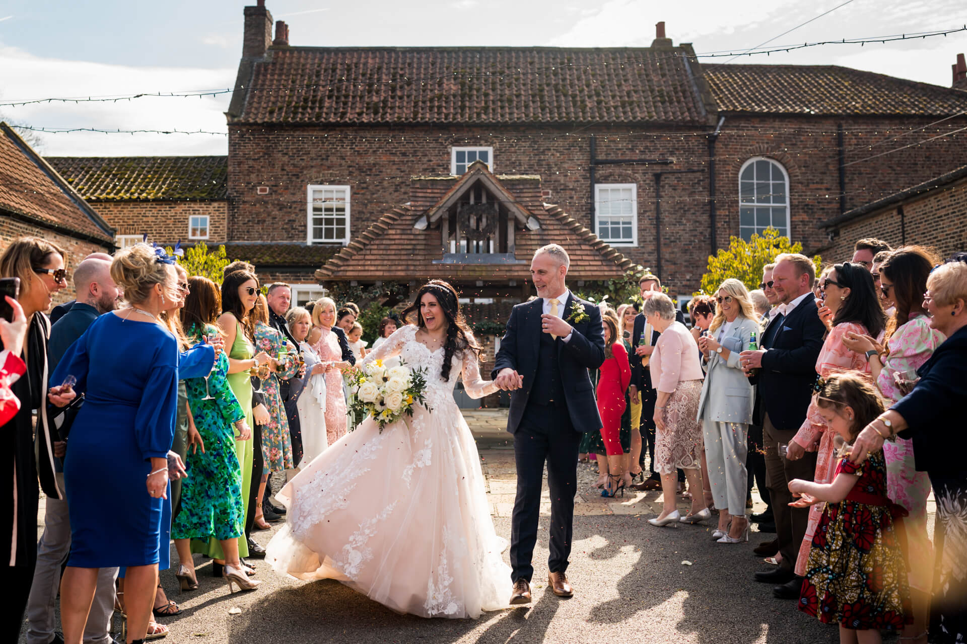 Bride and groom walking, guests throwing confetti outdoors at Hornington Manor