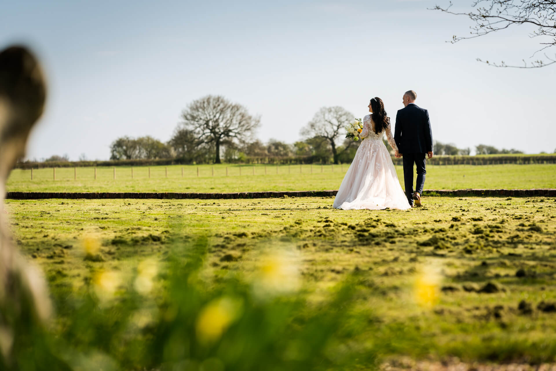 Bride and groom walking in sunny countryside field at Hornington Manor