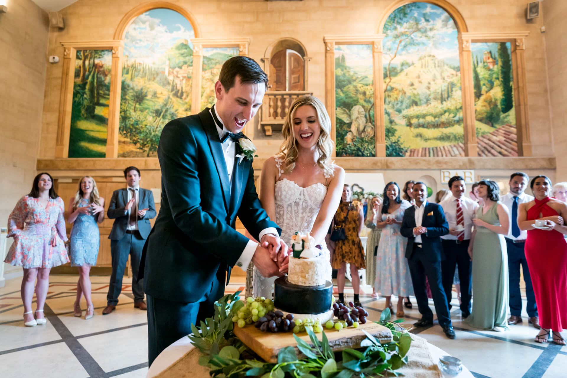 Bride and groom cutting wedding cake with guests watching.