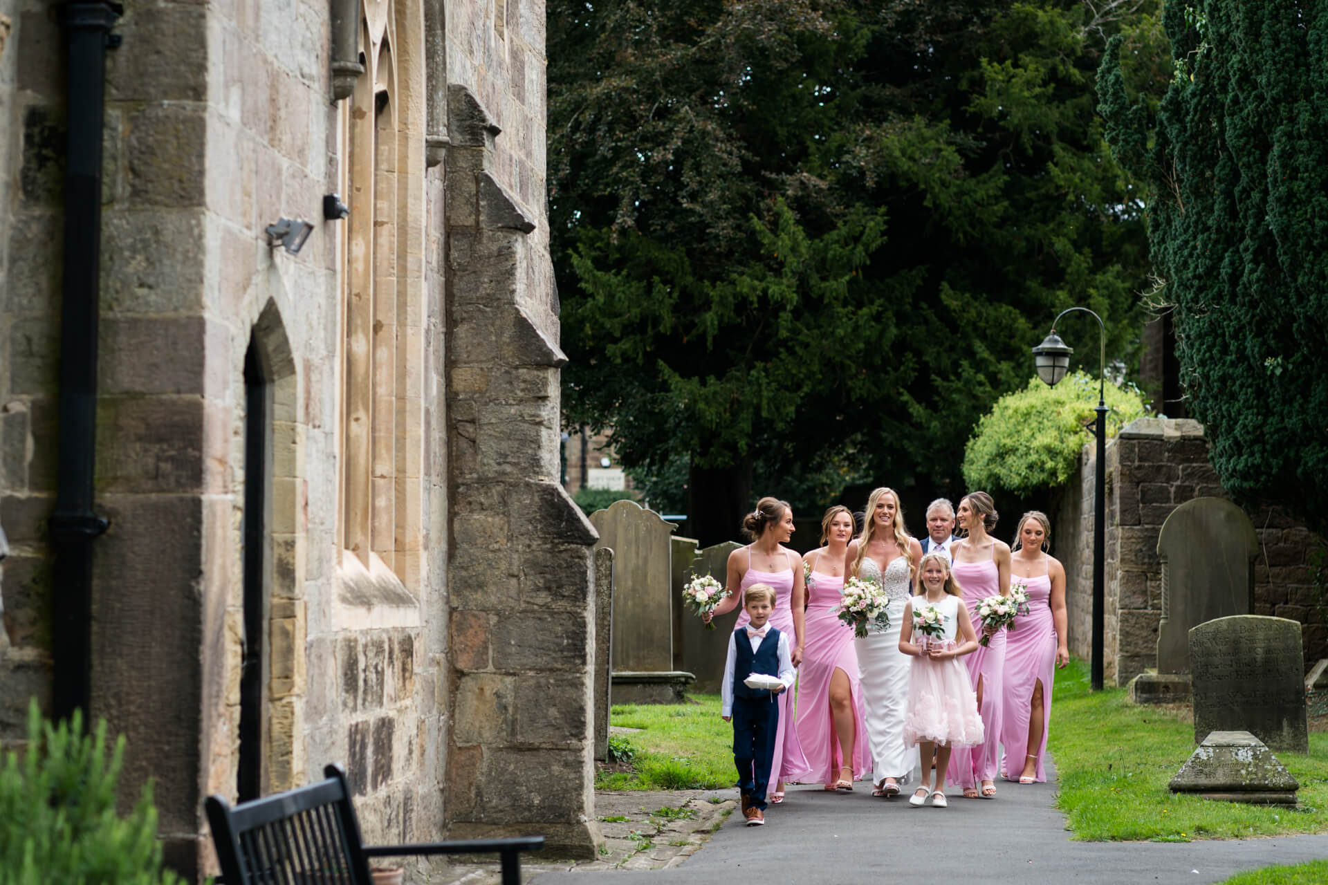 Bridal party walking by churchyard in pink dresses.