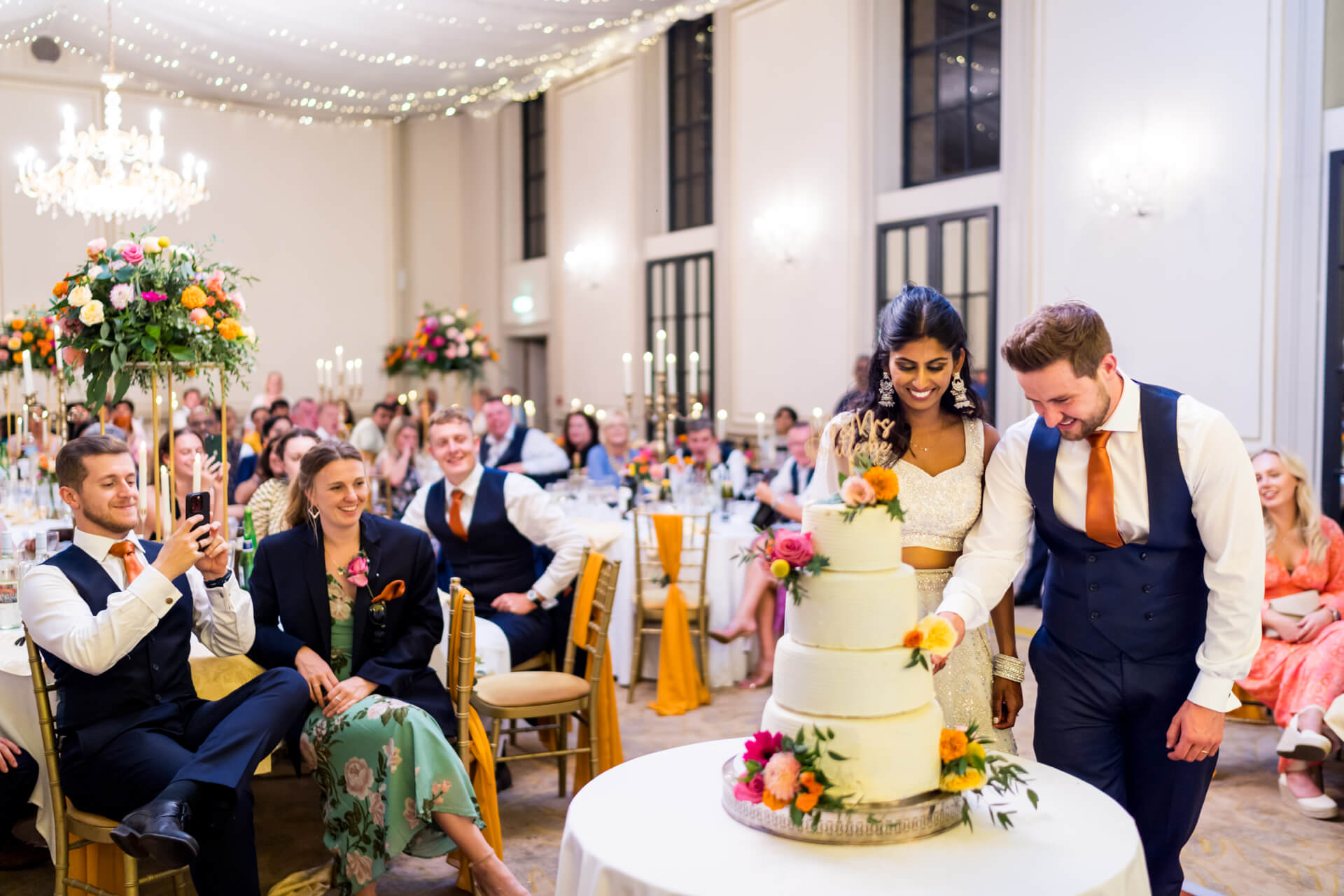 Couple cutting cake at festive wedding reception at Rise Hall