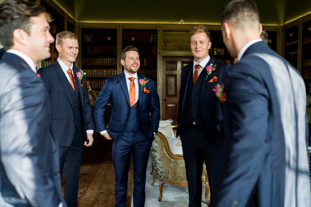 Groomsmen in suits smiling in ornate library at Rise Hall