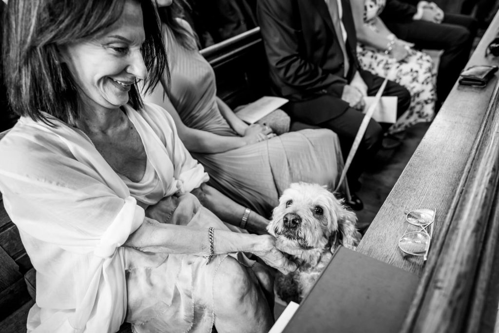 Woman petting dog whilst sat down in church, smiling, black and white photo.