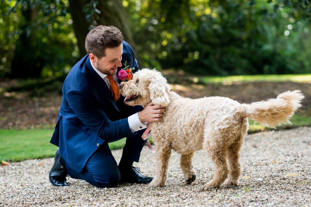 Groom petting dog at outdoor wedding.