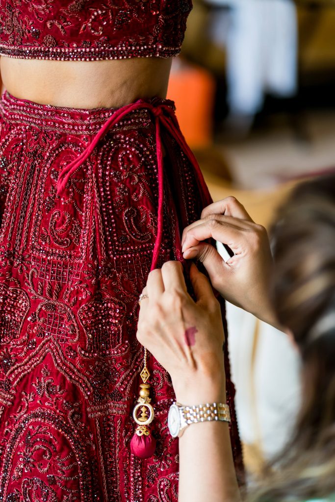 Person adjusting intricate red embroidered dress.