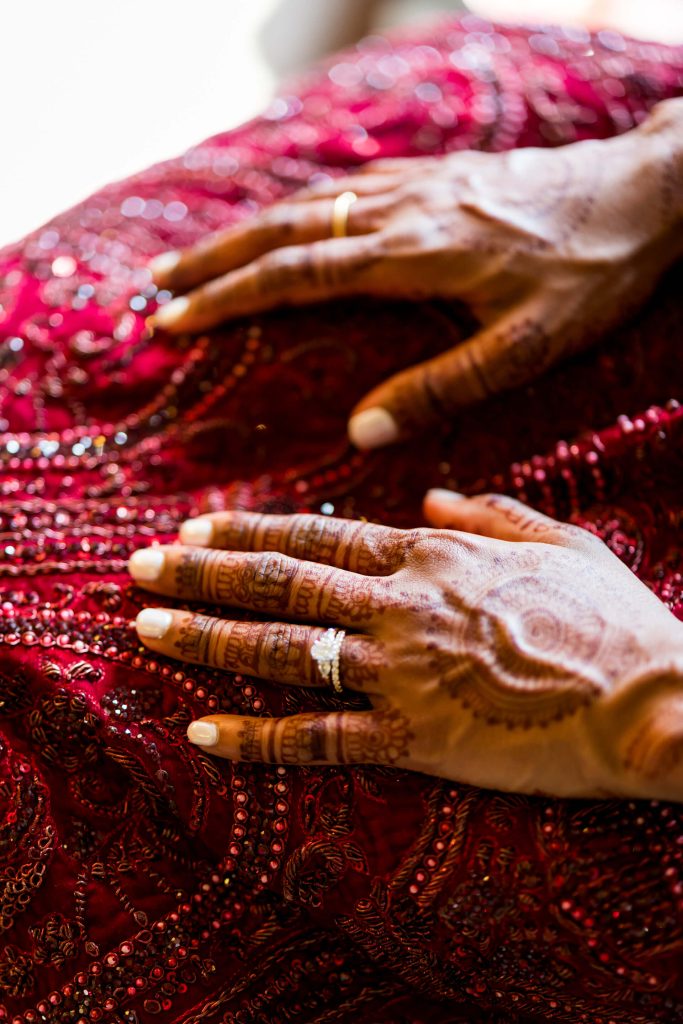 Henna-adorned hands over intricately embroidered red fabric.