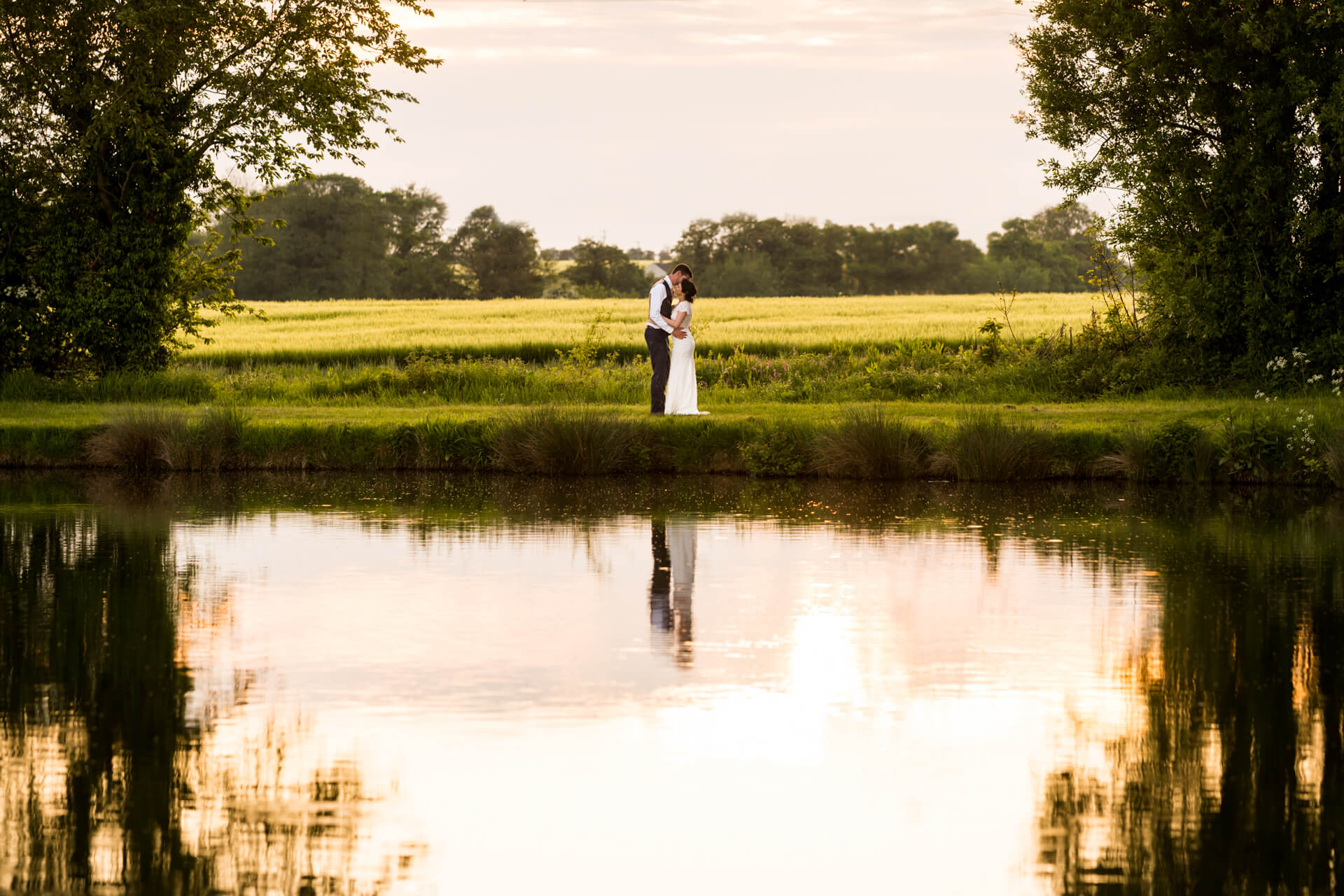 Couple embracing by serene lake at sunset at Low Osgoodby Grange