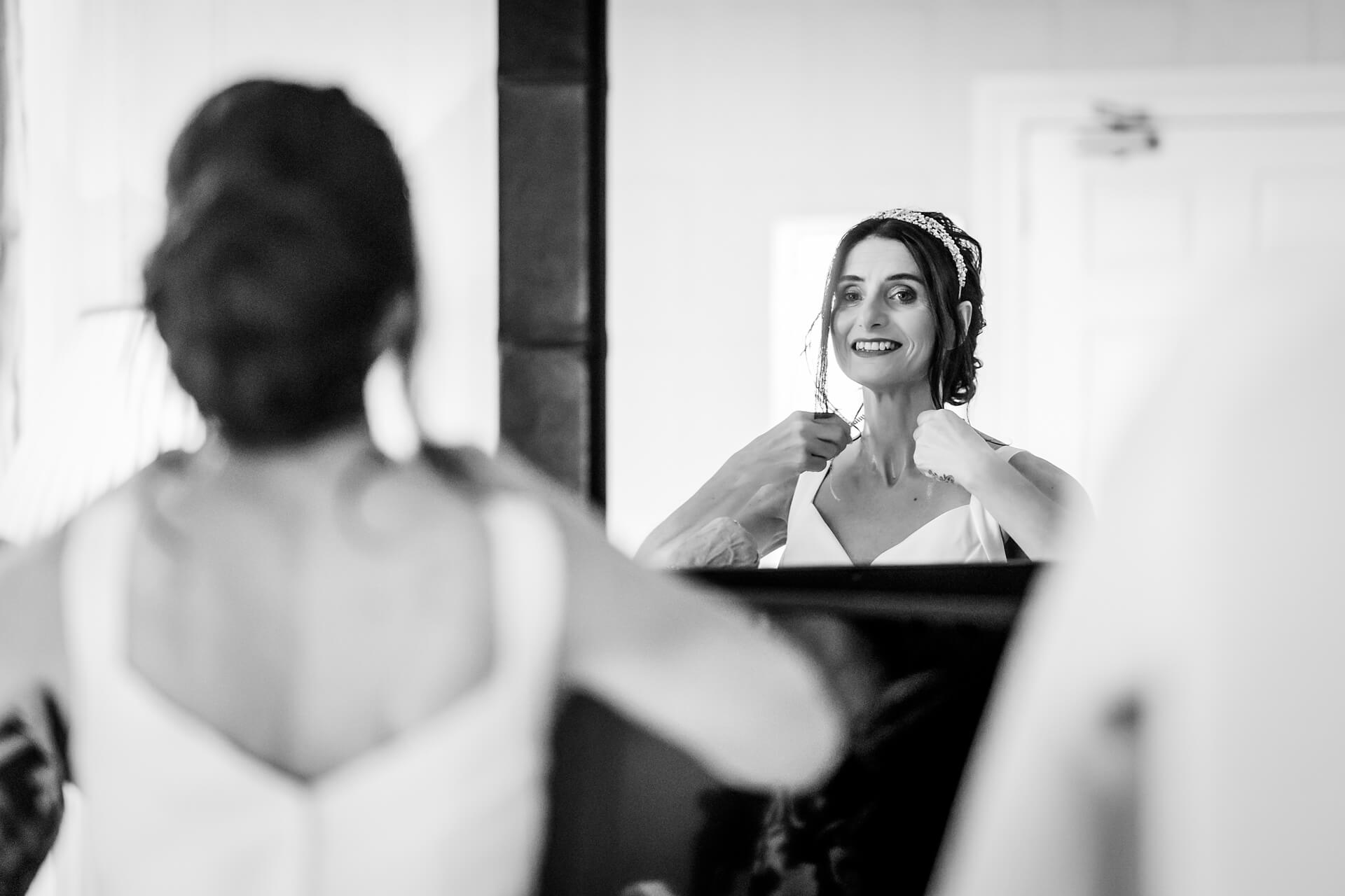 Bride adjusting earrings, reflection in mirror.