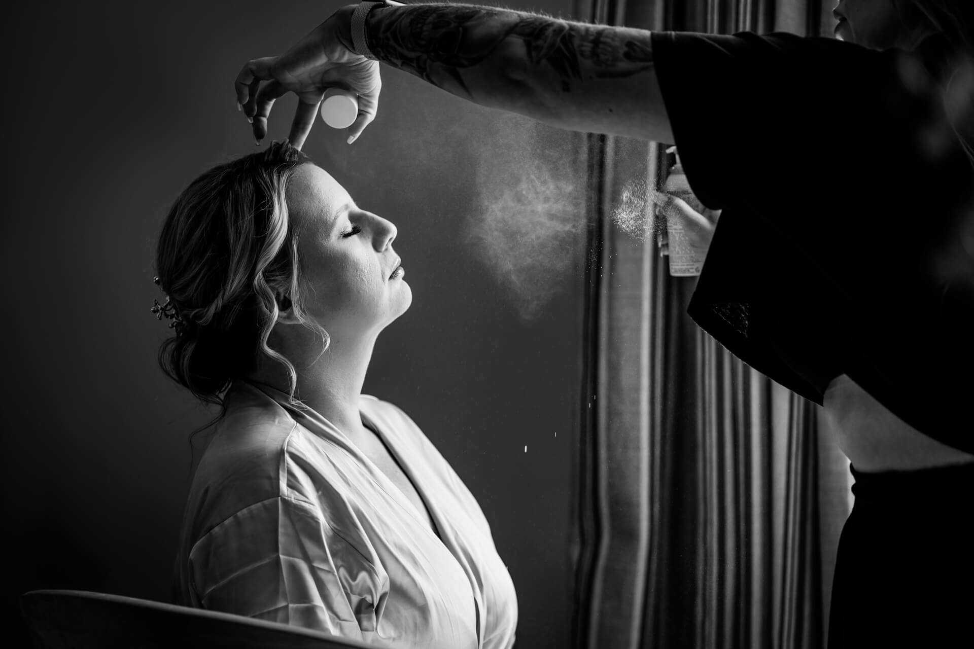 Bride getting hairspray by stylist in black and white.