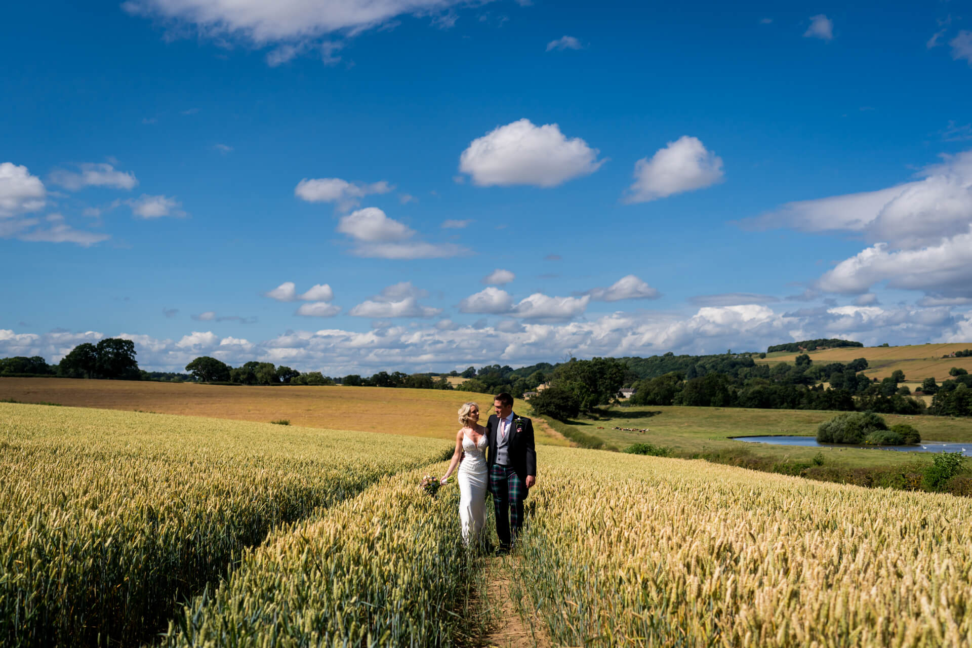 Couple walking in countryside wheat field on sunny day near The Yorkshire Wedding Barn