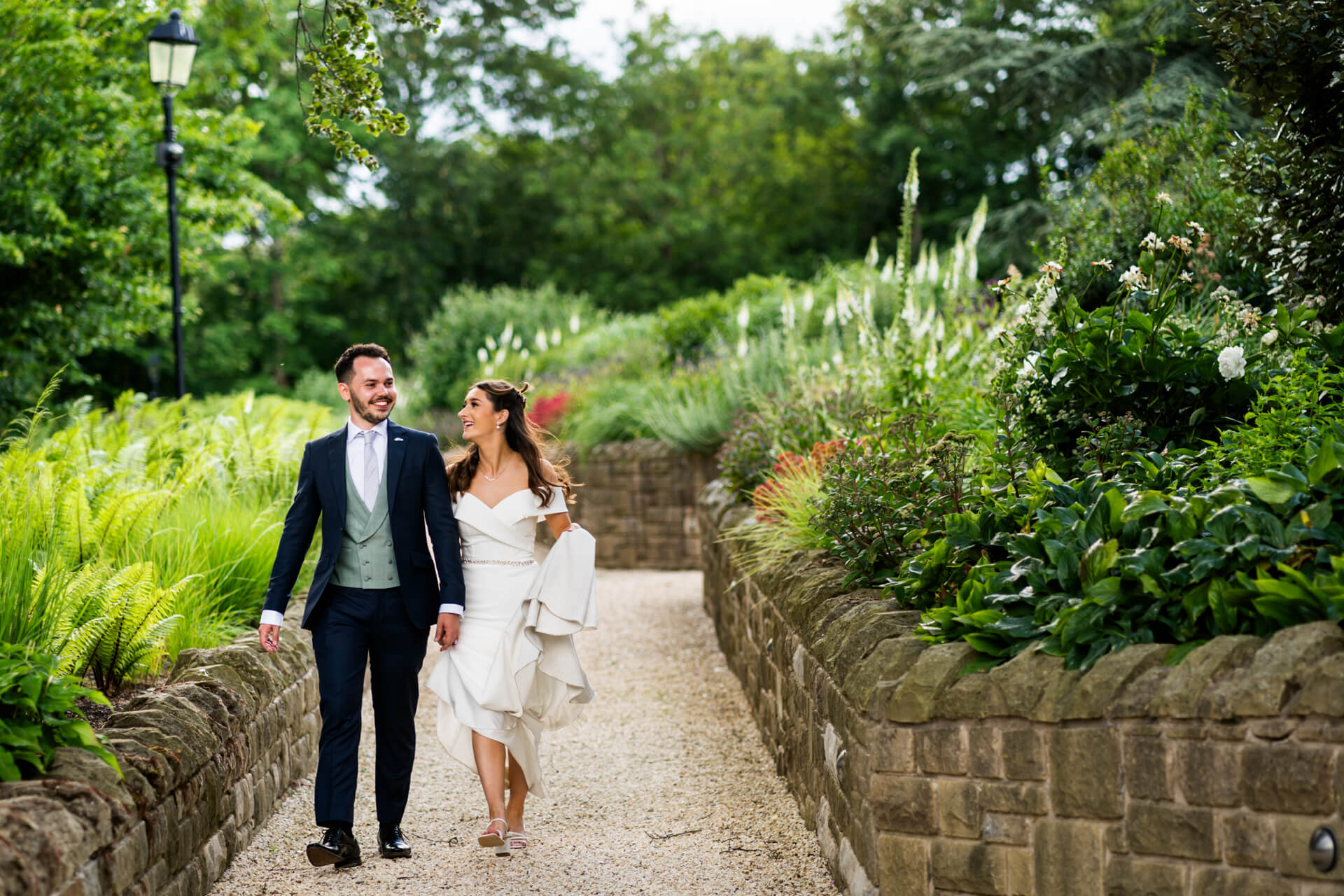Couple walking in lush garden paths Bowcliffe Hall , wedding attire.