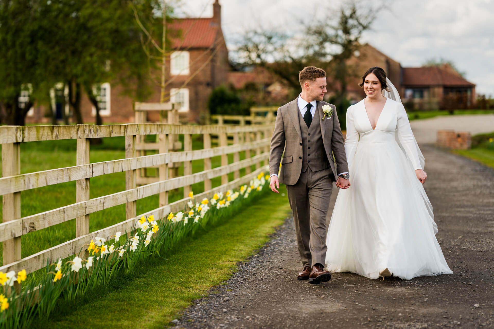 Couple walking by daffodils on rural wedding day at Thirsk Lodge Barns