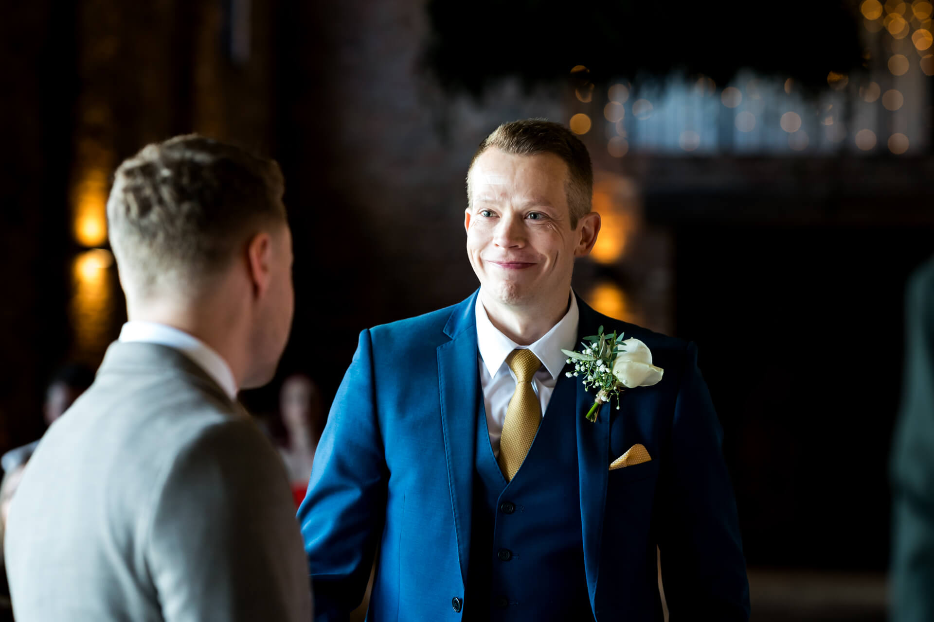 Groomsman in blue suit smiling at wedding reception.