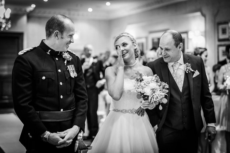 Bride wiping a tear from her eye as she sees the groom at the top of the aisle